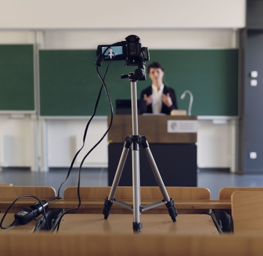 Lehrende steht vor Tafel und wird per Video aufgezeichnet