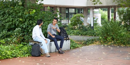Studierendenpaar im intensiven Gespräch auf einer Bank im Grünen