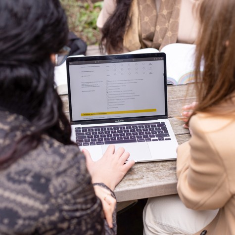 Zwei Studentinnen sitzen an einem Tisch und haben ein Laptop mit einem Online-Fragebogen geöffnet